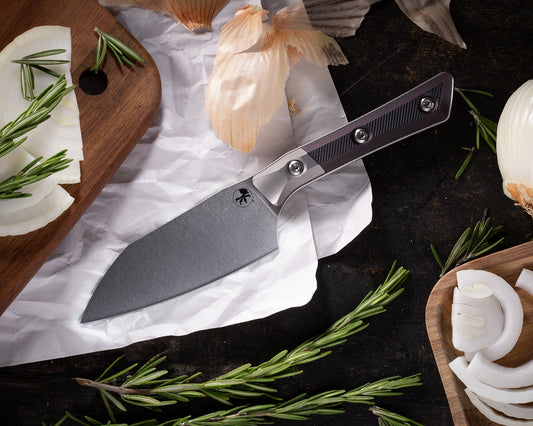 Santoku knife with black handle on parchment paper, onions, rosemary, and cutting board