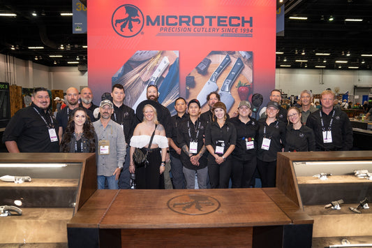 Microtech Knives team at convention booth with cutlery displays and branded backdrop