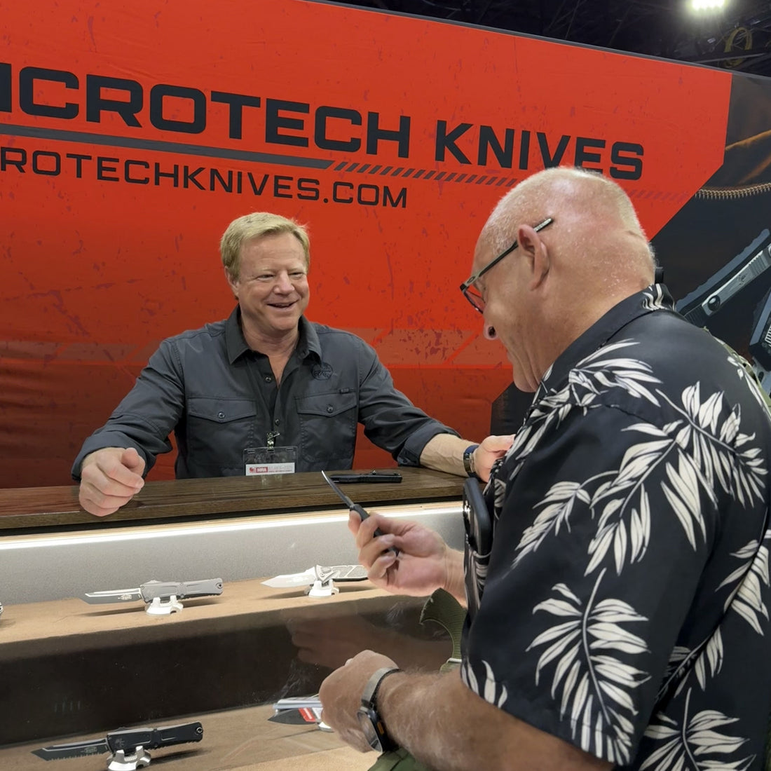 Two men talking at Microtech Knives booth with knife display case at trade show