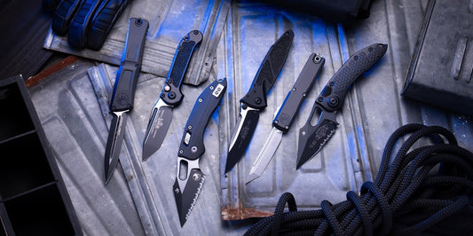 Assorted tactical folding knives displayed on metal surface with gloves and rope, outdoor gear