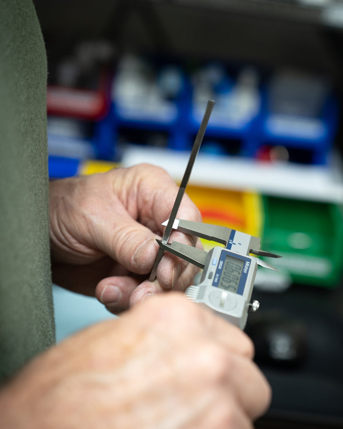 Close-up of hands using digital caliper to measure metal rod, quality control lab setting