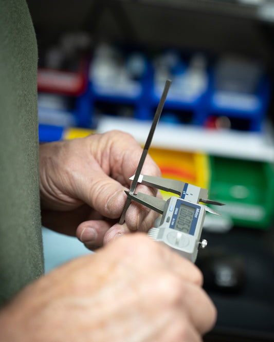Close-up of hands using digital caliper to measure metal rod, quality control lab setting