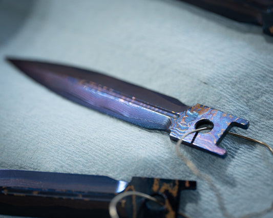 Blued steel knife blade with iridescent finish on light fabric background