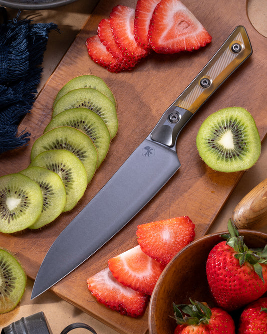 Microtech Culinary Utility Knife with ultem handle, DLC titanium bolsters and DLC stainless steel blade on a wooden cutting board and surrounded by fresh fruit. Premium professional kitchen knife for precision chopping and modern cooking.