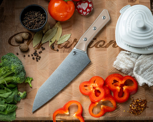 Microtech Culinary Chef Knife with coyote tan G10 handle and stonewashed stainless steel blade on a wooden cutting board surrounded by fresh vegetables and spices. Premium professional kitchen knife for precision chopping and modern cooking.