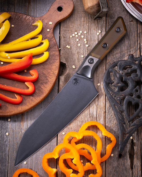 Microtech Chef Knife with DLC finish and ultem handle featuring Titanium bolster, displayed on rustic cutting board with sliced bell peppers.