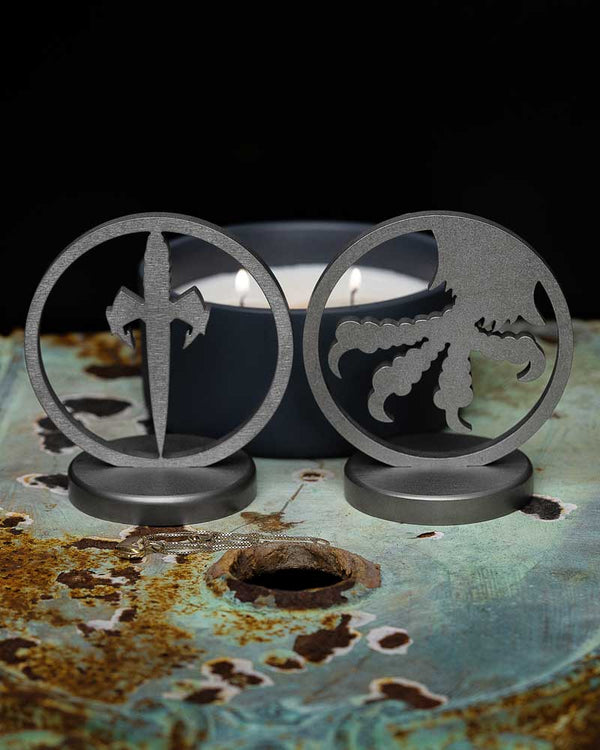 Metal desk stands with sword and octopus cutouts on a rustic table near a lit candle